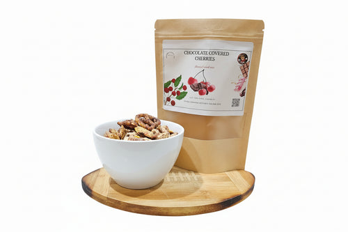 Bag of chocolate-covered cherries snack mix with a bowl of snacks on a wooden board against a white background