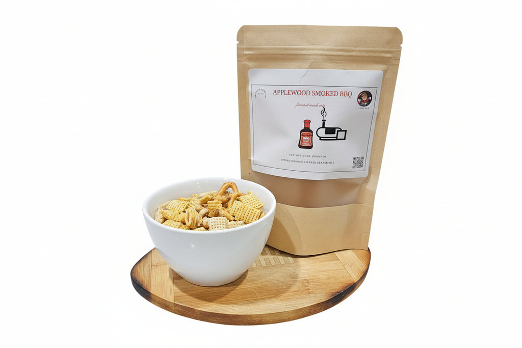 Bag of Applewood Smoked BBQ mix next to a bowl of gourmet snack mix on a wooden board with a white background