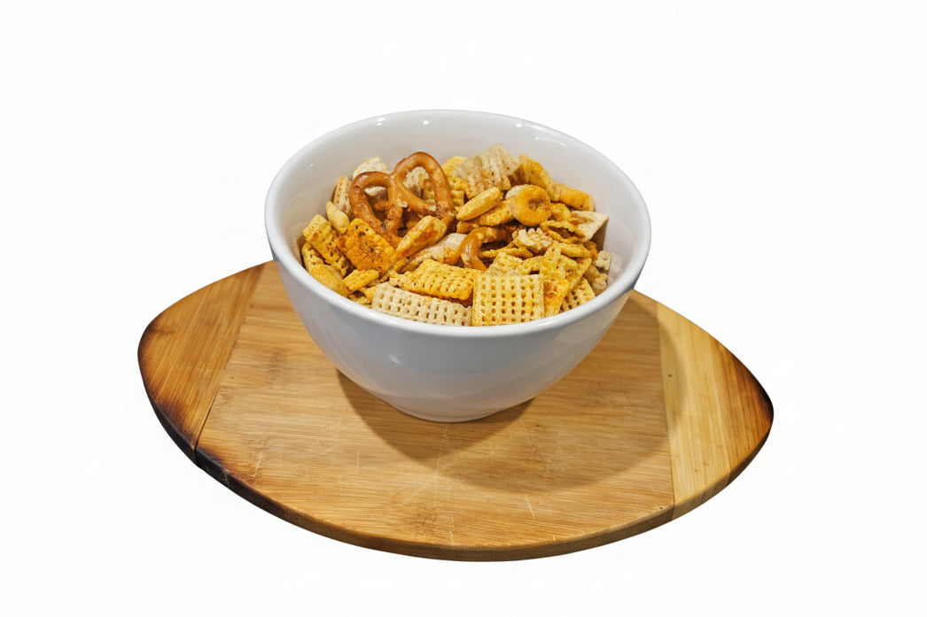 White bowl of buffalo gourmet snack mix on a wooden coaster with a white background